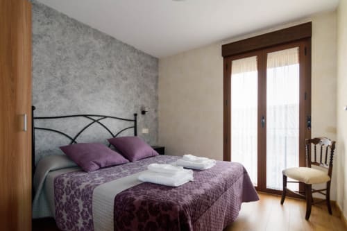 Dormitorio con ropa de cama morada, cabecero metálico y puertas de cristal en Tradición Rural, Nieva, España