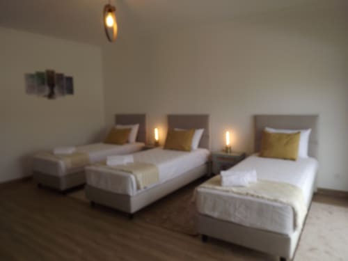Triple Room at Embaixada da Vila in Cascais with three beds, gold pillows, modern lighting, and garden views