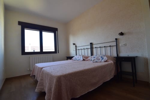 Luminoso dormitorio en Tradición Rural con cama de estructura metálica, ropa de cama beige y ventanas con vistas a Nieva