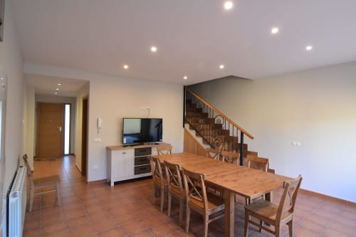 Área de comedor y sala de estar integrada en Tradición Rural en Nieva con mesa de madera, televisor y escalera.