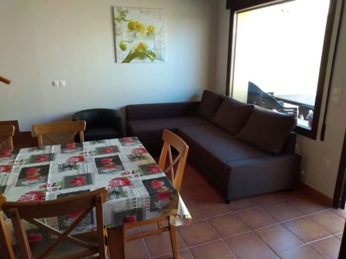 Acogedora sala de estar en Tradición Rural de Nieva con sofá oscuro, mesa de comedor de madera y cuadro de flores amarillas
