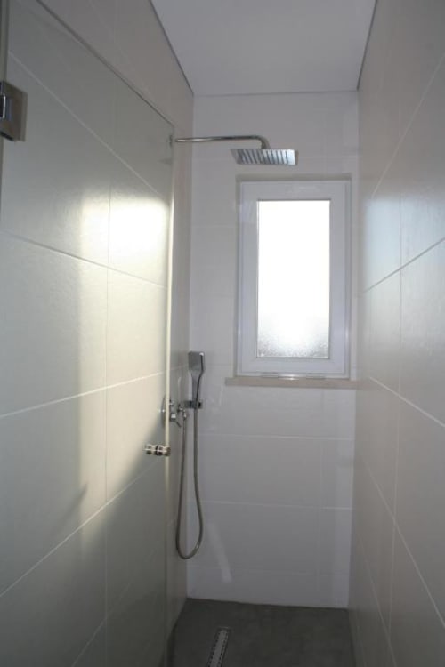 Modern bathroom with white tile walls, rainfall showerhead, and window at Recantus Comporta hotel in Comporta, Portugal