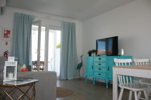 Egret Apartment living area at Recantus Comporta with turquoise dresser, TV, white dining chairs, and garden view through