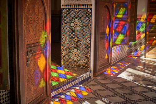 Colorful stained glass light patterns on ornate wooden doors and zellige tile floor at Riad Madinina, Marrakech