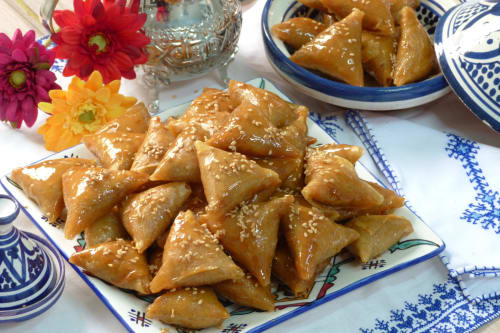 Pâtisseries dorées au sésame servies au Riad Madinina de Marrakech avec fleurs colorées et vaisselle marocaine traditionnelle.