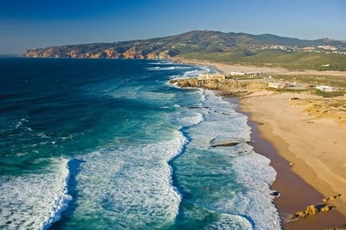 Coastal cliffs and sandy beach with turquoise waves near Cascais, Portugal - Embaixada da Vila