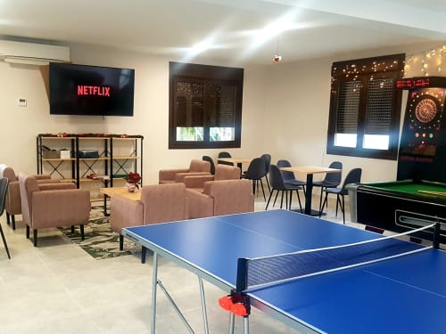 Sala de entretenimiento equipada con mesa de ping-pong, pantalla con acceso a Netflix, área de asientos cómodos y juegos recreativos como dardos y futbolín. El espacio está decorado con luces y es ideal para el esparcimiento y la socialización en grupo. Este ambiente ofrece diversas opciones de ocio para disfrutar en interiores.