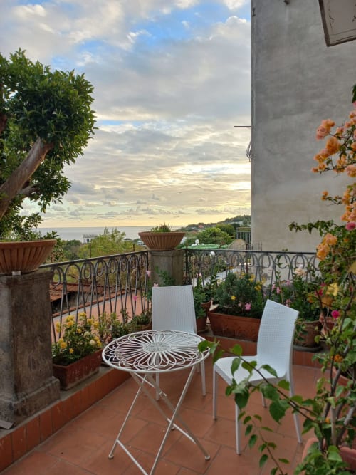 Terrazza di La Suite del Giardino a Napoli con vista mare, arredi bianchi, fiori in vaso e ringhiera decorativa