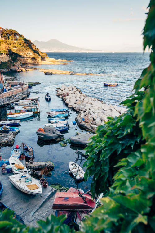 Coloratissime barche da pesca in un tranquillo porto costiero con il Vesuvio in lontananza, vicino a Napoli