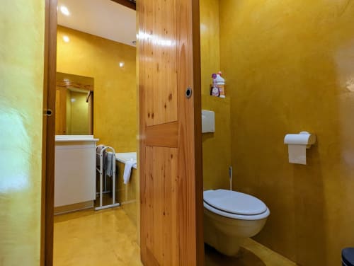 Salle de bain jaune lumineux avec poutres en bois, toilettes blanches, lavabo et porte-serviettes aux Chambres d'hôtes le Grand Bienfaisy