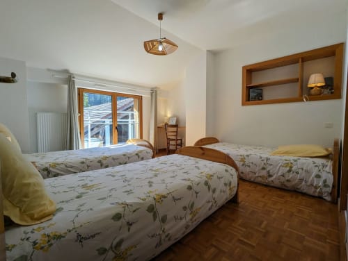 Chambre lumineuse avec trois lits simples, poutres en bois et balcon avec vue sur le jardin aux Chambres d'hôtes le Grand Bienfaisy