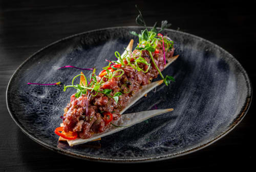 Elegant beef tartare dish on dark plate at Brooklyn House, Southgate London, garnished with microgreens and microradish