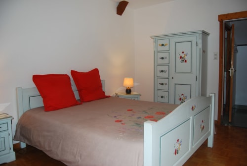 La chambre Poppy aux Chambres d'hôtes le Grand Bienfaisy à Remiremont dispose d'un lit blanc avec des oreillers rouges et une literie florale.
