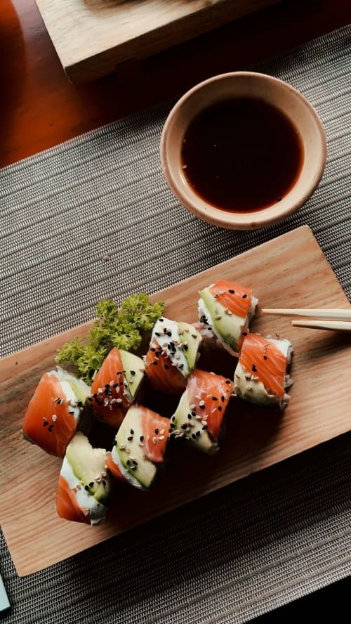 Salmon sushi rolls with sesame seeds and cucumber on wooden board at Brooklyn House, London