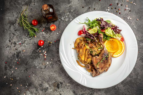 Grilled meat with roasted potatoes, fresh salad, and orange slices on white plate at Brooklyn House, Southgate London