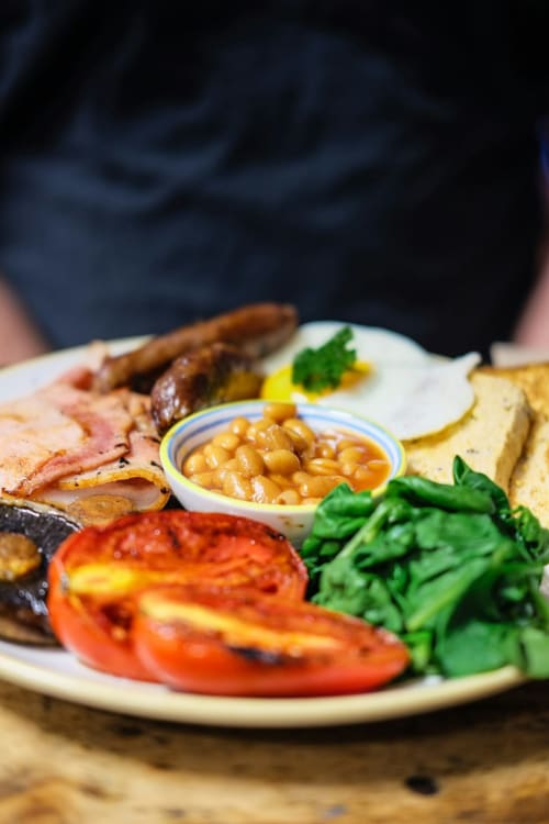 Full English breakfast at Brooklyn House B&B in Southgate, London featuring bacon, grilled tomato, beans, and fresh greens