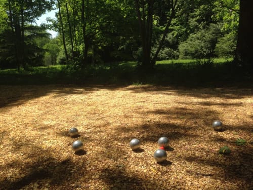 Pétanque game at Domaine de l'Ocrerie, boules court with metal balls on gravel surrounded by lush green forest in Pourrain