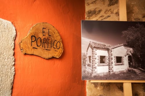 Letrero de la habitación El Porticó en la casa rural Can Gat Vell en Gerona, con fotografía antigua en blanco y negro del edificio de piedra