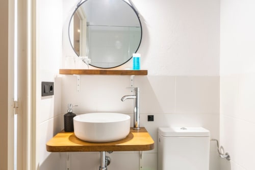 Baño moderno en el B&B Can Gat Vell de Girona con lavamanos redondo blanco, mueble de madera, espejo circular e inodoro.