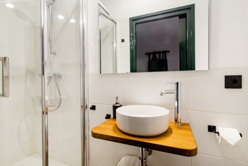 Baño moderno en la casa rural Can Gat Vell con lavabo redondo blanco sobre encimera de madera y ducha tipo lluvia, Girona