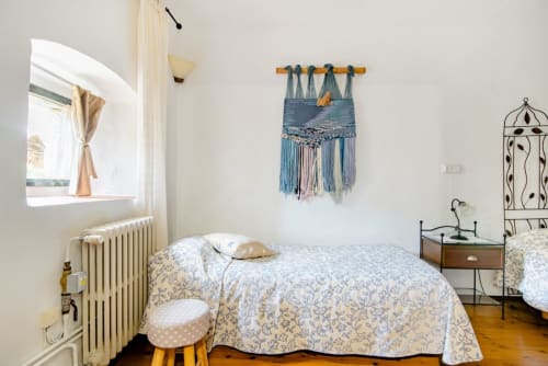Acogedora habitación en Can Gat Vell B&B en Girona con tapiz macramé azul, ropa de cama con estampados y suelo de madera.