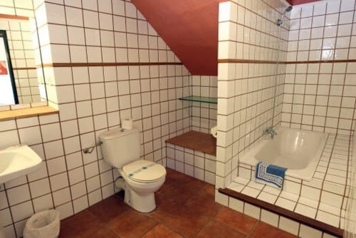 Baño de cabaña con azulejos tipo metro color crema, suelo rojo marrón, inodoro blanco y bañera en Can Gat Vell, Girona