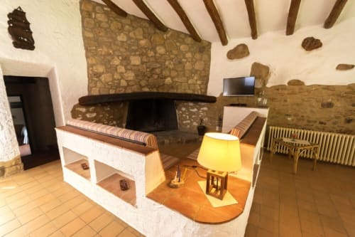 Salón rústico con chimenea de piedra, vigas de madera y lámpara amarilla en la casa rural Can Gat Vell en Girona, Cataluña