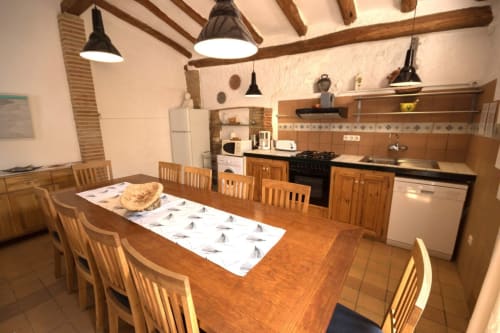 Amplia cocina-comedor de la casa rural Can Gat Vell en Girona con mesa de madera, sillas, electrodomésticos y vigas vistas