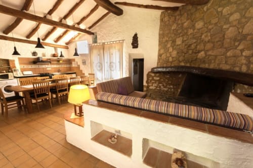 Sala de estar diáfana con chimenea, cocina y sofá de rayas en la casa rural Can Gat Vell en Girona