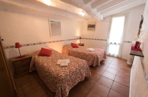 Dormitorio luminoso con dos camas individuales, almohadas rojas, suelo de barro cocido y puerta con vistas al jardín en la casa rural Can Gat Vell en Girona