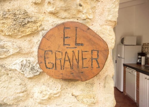 Señal circular de madera que dice 'EL GRANER' montada en la pared de piedra de la casa rural Can Gat Vell en Girona, Cataluña