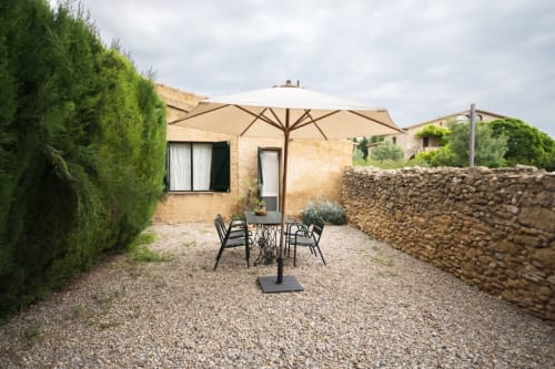 Terraza con sombrilla beige y asientos en Can Gat Vell en Girona, Empordà, rodeada de muros de piedra y vegetación