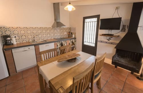Cocina abierta y comedor de la casa rural Can Gat Vell en Girona, con mesa de madera, chimenea y comodidades modernas