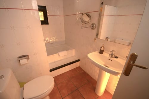Baño moderno con azulejos blancos, suelo rojo, lavabo, inodoro y ducha en la casa rural Can Gat Vell, Girona