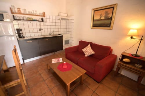 Acogedora sala de estar de la casa rural Can Gat Vell en Girona con sofá rojo, mesa de madera, cocina y chimenea