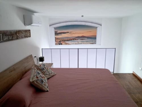 Camera moderna di La Suite del Giardino a Napoli con vista sul tramonto costiero, biancheria bordeaux e testata metallica