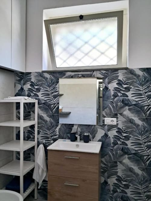 Bagno moderno di La Suite del Giardino a Napoli con carta da parati a motivi tropicali, mobile lavabo in legno e finestra con vista sul giardino