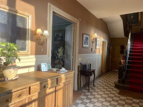 Élégant couloir du Château de Vaux Morvan avec buffet en bois, miroir, appliques et carrelage à damier près de l'escalier