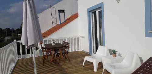 Varanda do Apartamento Flamingo no Recantus Comporta com mesa de jantar, espreguiçadeiras, guarda-sol e vista para o jardim