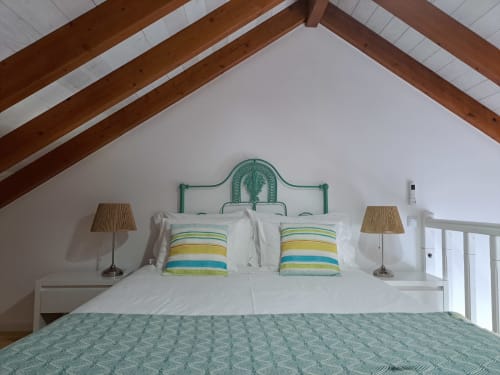 Quarto luminoso no Apartamento Flamingo em Recantus Comporta com cabeceira de metal verde, almofadas listradas e vigas aparentes