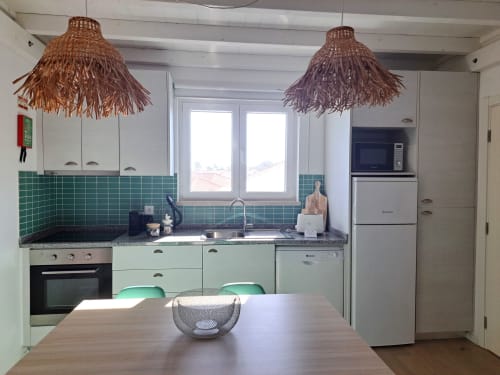 Modern kitchen in Flamingo Apartment at Recantus Comporta with mint green cabinets, green tile backsplash, and woven pendant
