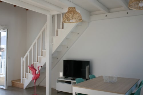 Interior moderno do apartamento Recantus Comporta com escada branca, luminária de teto trançada, TV e sala de jantar em madeira