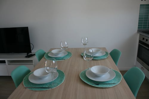Mesa de jantar preparada para quatro pessoas no Recantus Comporta com marcadores turquesa, louça branca e taças de vinho em Flamingo