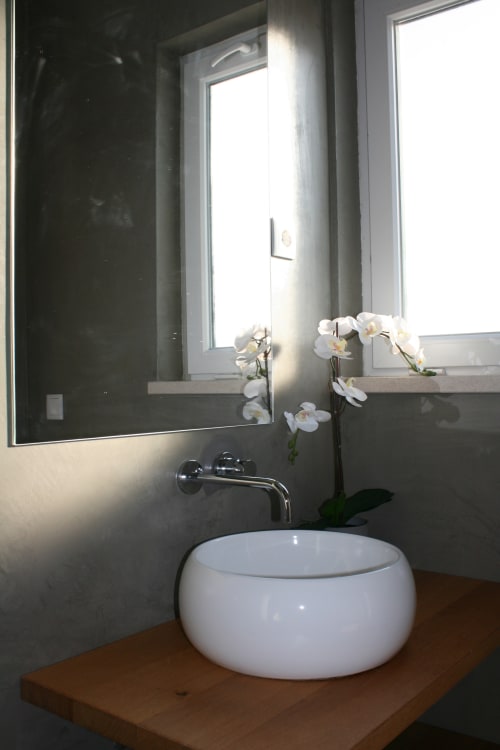 Banheiro moderno com cuba branca em bancada de madeira, flores de orquídea, espelho e janela no hotel Recantus Comporta,