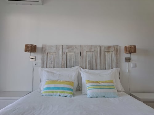 Quarto iluminado em Recantus Comporta com cabeceira de madeira caiada, almofadas listradas e luminárias laterais de palha