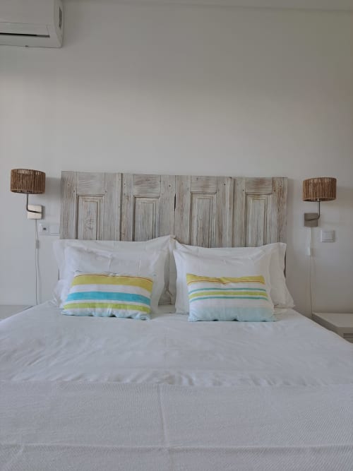 Quarto luminoso no Recantus Comporta com cabeceira de madeira caiada, roupa de cama branca e almofadas com listras coloridas