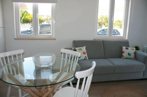 Sala de estar luminosa no Apartamento Dolphin em Recantus Comporta com sofá cinzento, mesa de jantar em vidro, cadeiras brancas e jardim