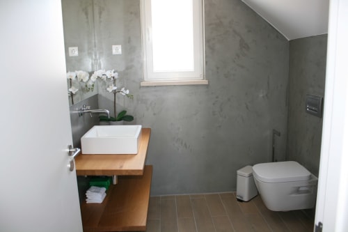 Banheiro moderno no Apartamento Dolphin em Recantus Comporta com cuba suspensa, orquídeas brancas e acabamentos contemporâneos