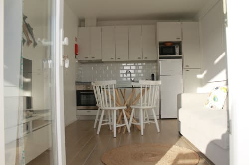 Zona moderna de cozinha-sala de refeições em Recantus Comporta com armários brancos, mesa de jantar e luz natural abundante