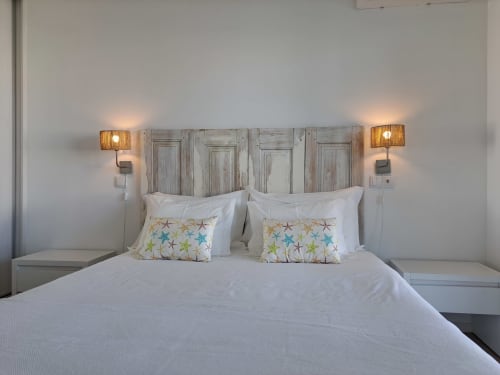 Bright bedroom at Recantus Comporta with white linens, starfish pillows, wooden headboard, and wall sconces